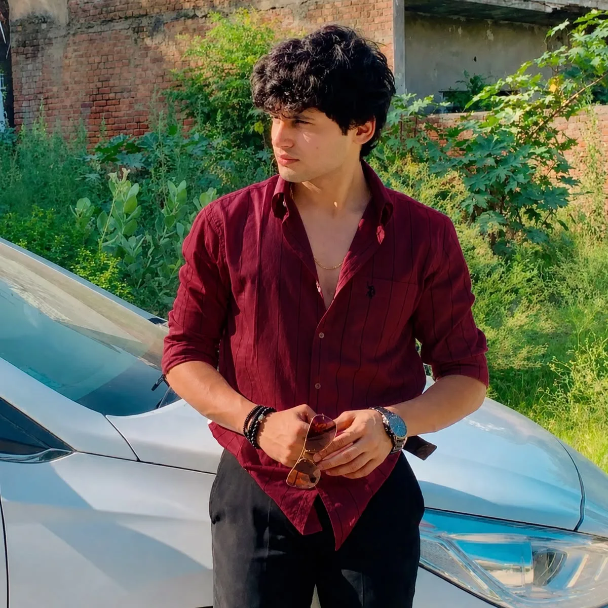 A young man stands confidently in front of a sleek white car