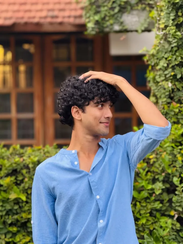 Candid Outdoor Side-Profile Portrait of Young Man with Curly Hair Resting Hand on Head