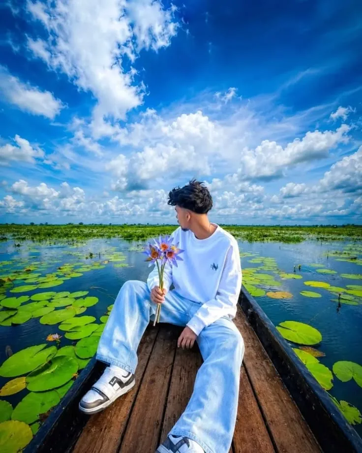 Young Man Sitting in Wooden Boat on Water Lily Lake Under Bright Sky