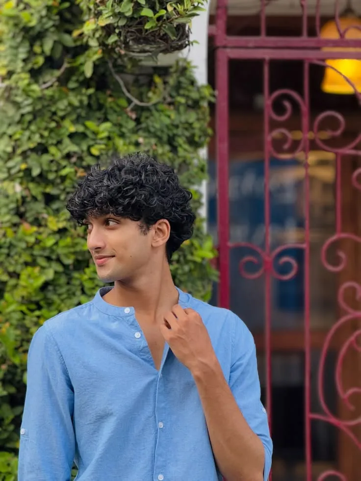 Candid Outdoor Side-Profile Portrait of Young Man with Curly Hair Adjusting Collar