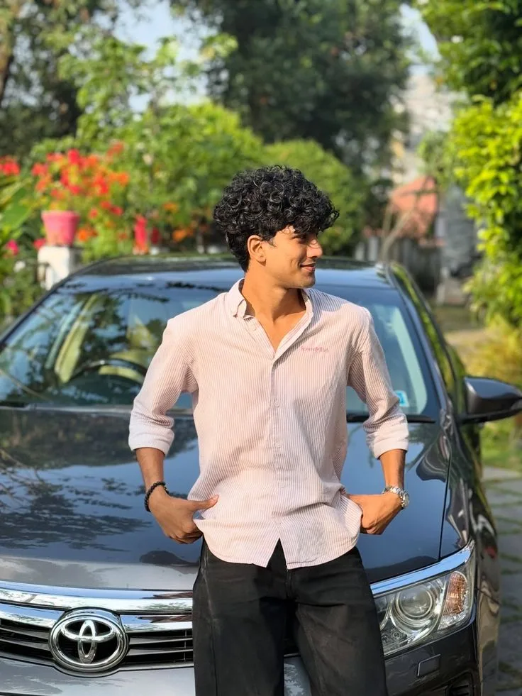 Candid Young Man in Pink Striped Shirt Leaning on Grey Car in Outdoor Sunshine