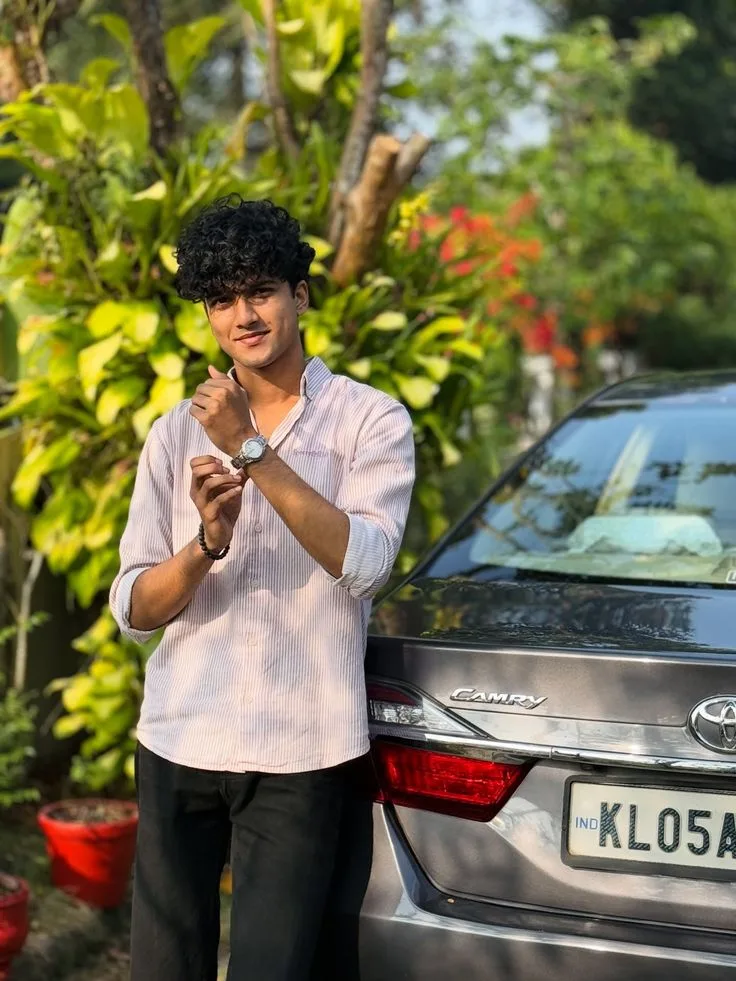 Candid Young Man in Pink Striped Shirt Adjusting Wristwatch Beside Grey Camry Car