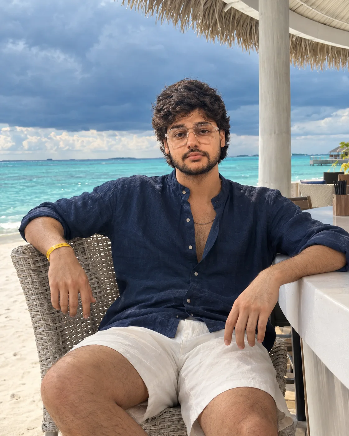 A polished tropical-resort portrait with rich navy linen, crisp white sand and dramatic cloud.