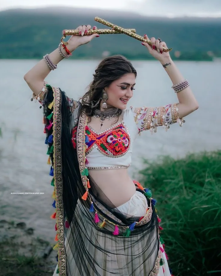 Festive Navratri Garba Portrait of Young Woman with Golden Dandiya Sticks by Lakeside