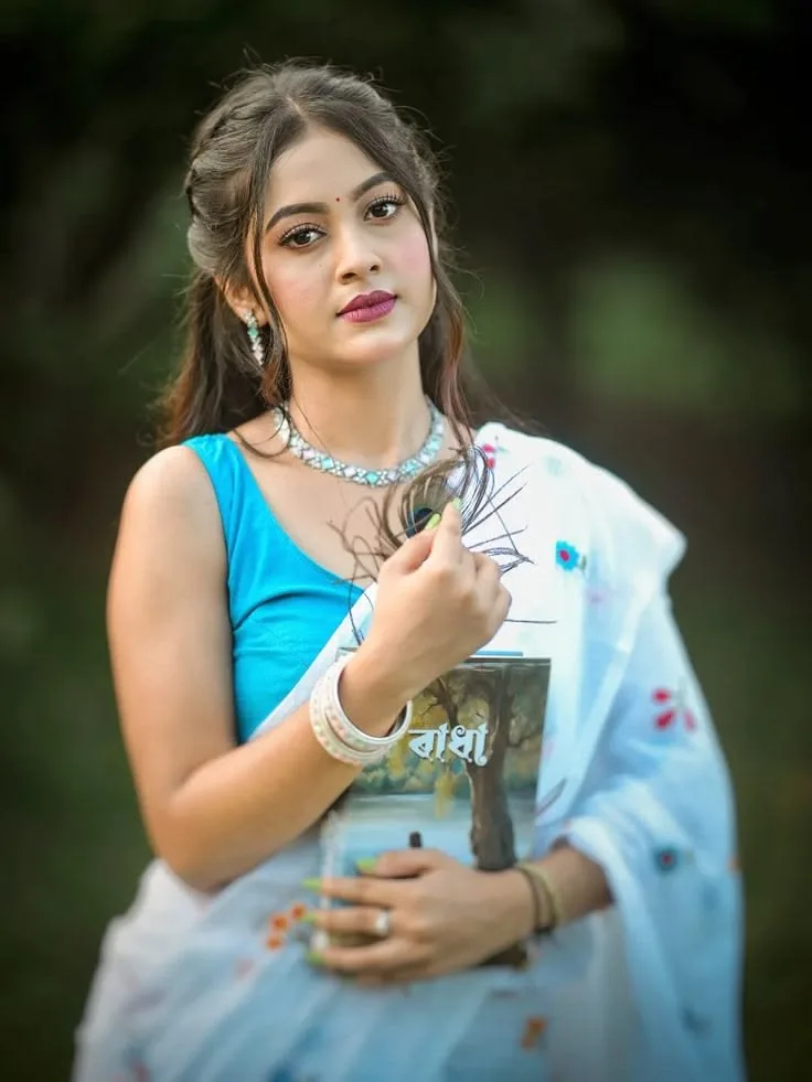 Candid Woman in Sky Blue Blouse and White Saree Holding Bengali Book and Peacock Feather