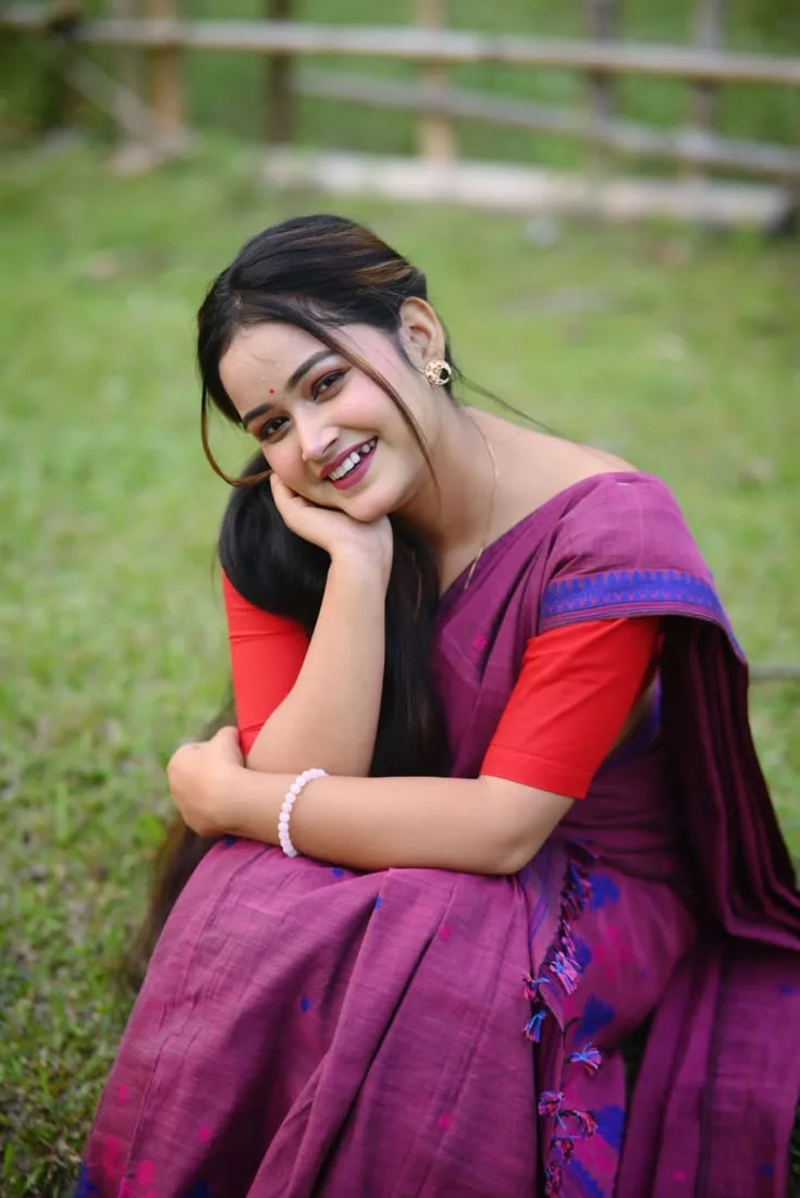Candid Young Woman in Plum Silk Saree Crouching on Green Grass with Red Blouse