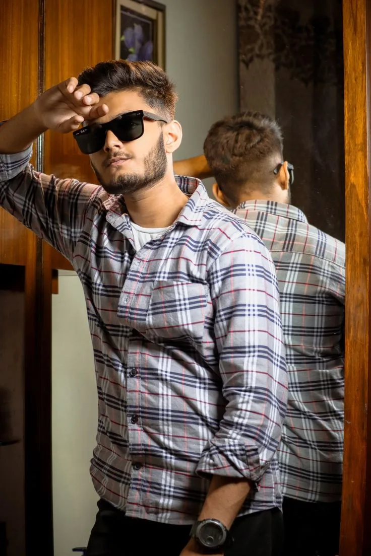 Candid Young Man in Plaid Flannel Shirt and Sunglasses Leaning Against Mirrored Wardrobe