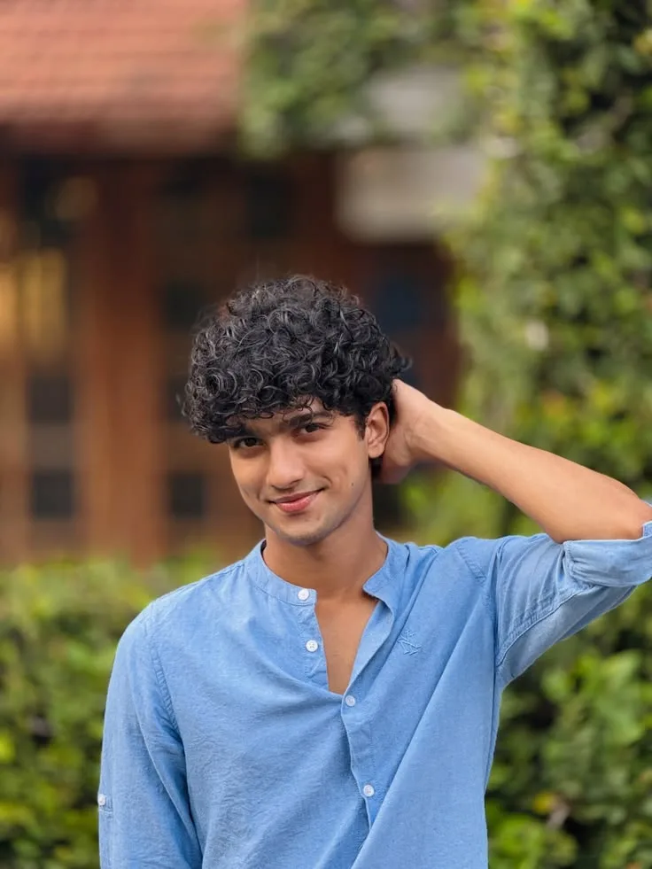Candid Outdoor Portrait of Young Man with Curly Fringe in Light Blue Linen Shirt
