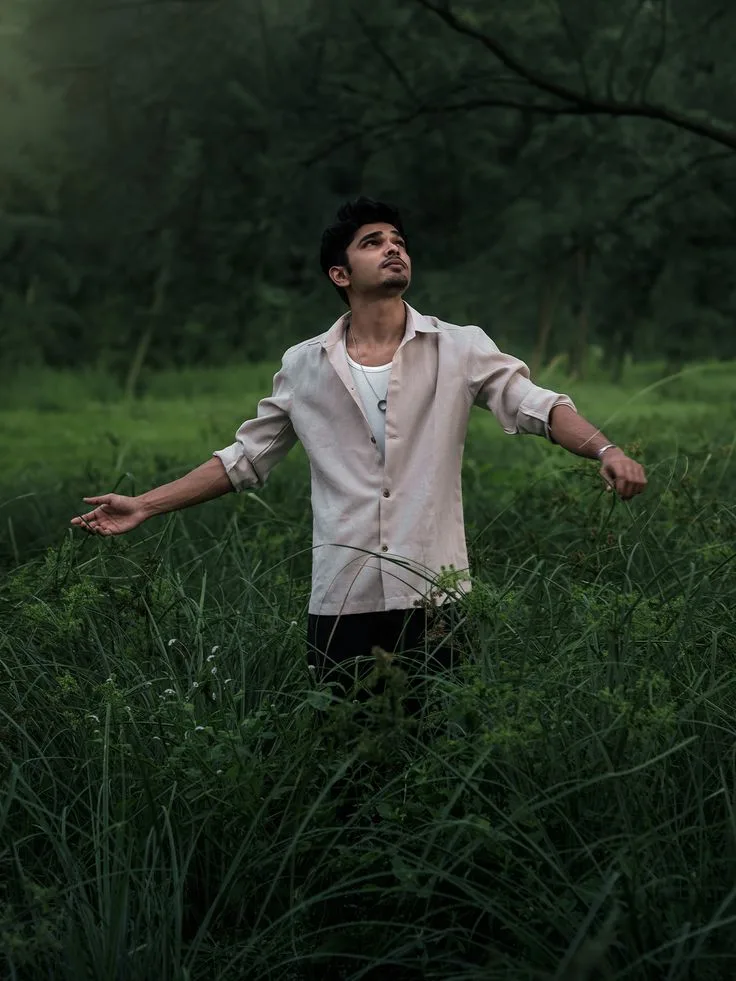 Candid Young Man in Linen Shirt with Outstretched Arms in Lush Tall Grass