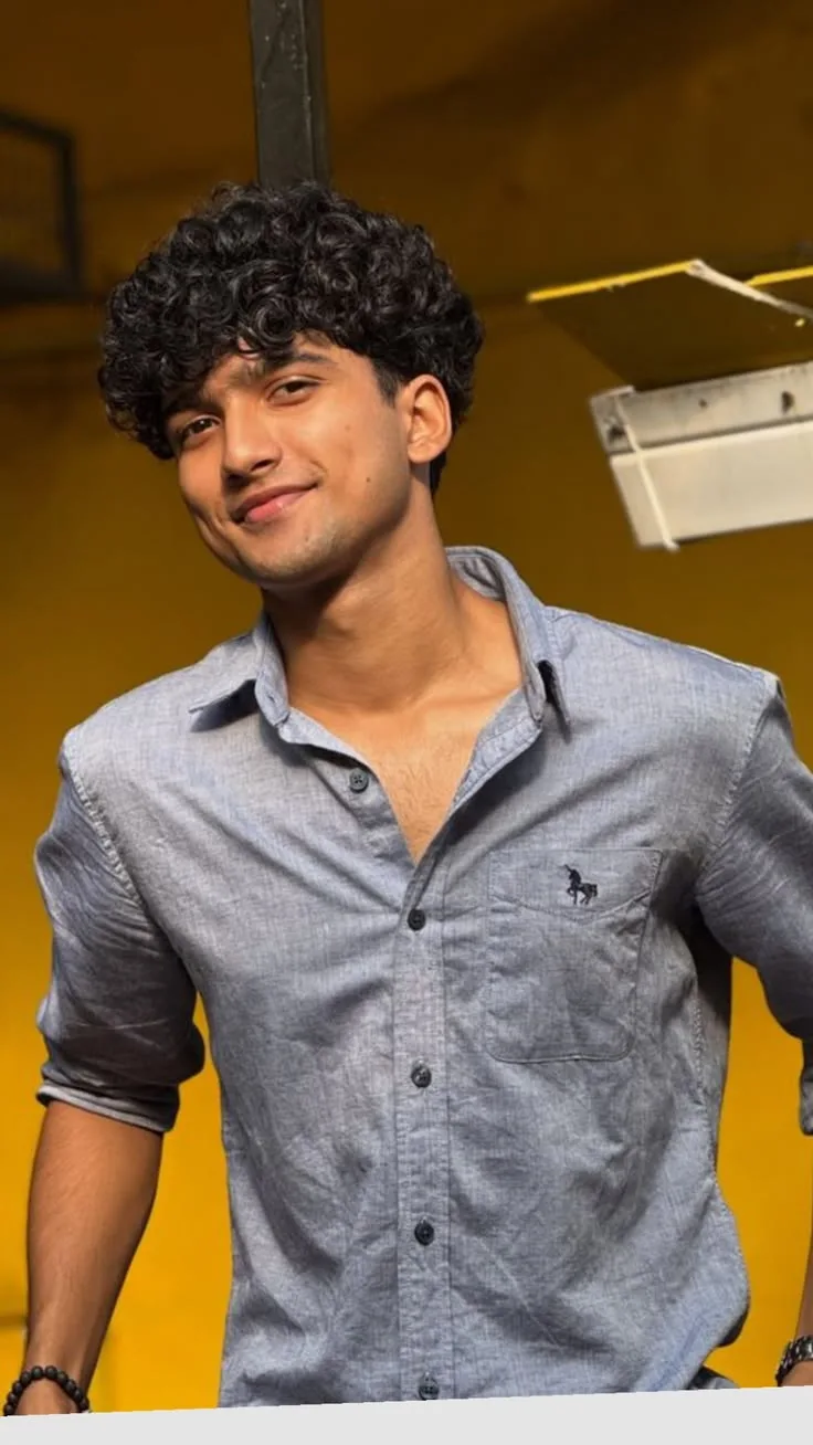 Candid Young Man in Grey Chambray Shirt with Dimpled Smile Against Yellow Wall