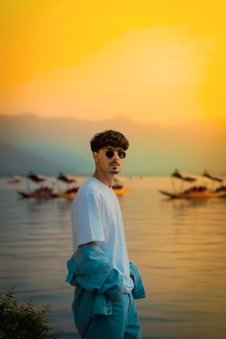 Candid Young Man in Denim Outfit and Round Sunglasses by Sunset Lake with Shikaras