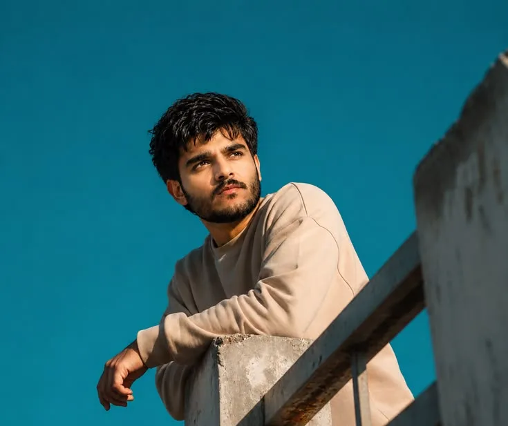 Candid Young Man in Beige Sweatshirt Leaning on Concrete Balcony Railing
