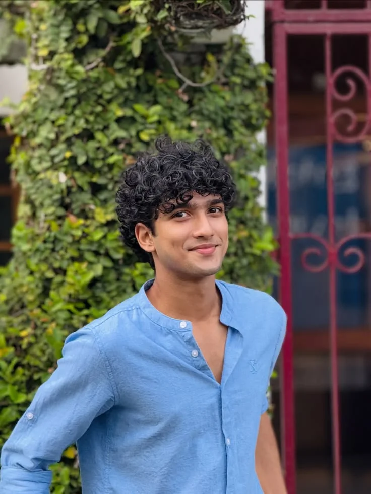 Candid Outdoor Portrait of Young Man with Curly Fringe in Blue Linen Shirt Smiling